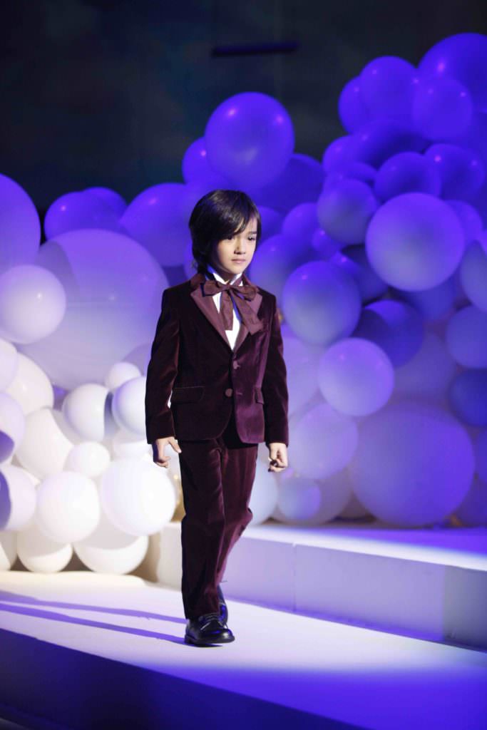 Beautiful velvet burgundy suit for boys fashion against a background of hundreds of white balloons at the Il Gufo winter 2017 show